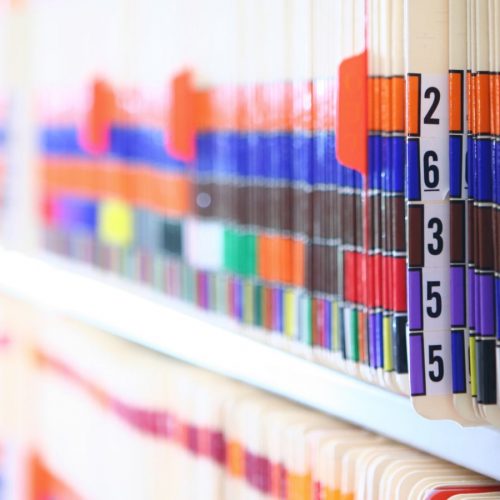 Color-coded medical record folders organized on shelves in a healthcare office.