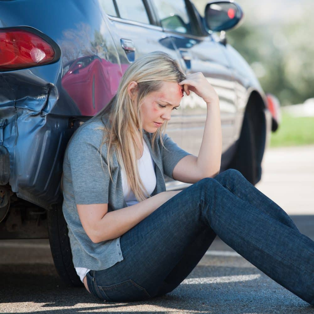 An injured woman leaning against her car after an accident.