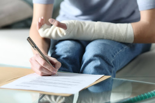 An individual with their arm in a cast after an accident signs documents related to their Maine personal injury claim.