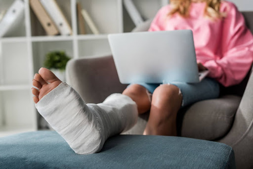A woman with her foot in a cast reviews accident-related medical bills on her laptop.