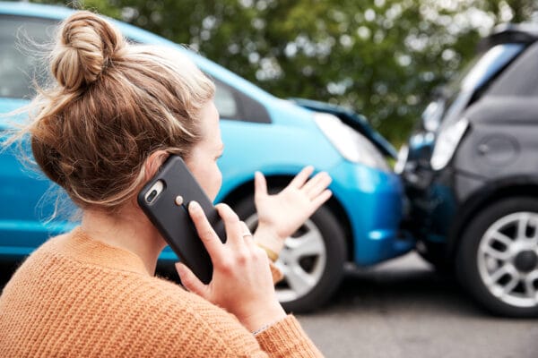 A woman calls for help after a rear-end car accident, standing beside two damaged vehicles.