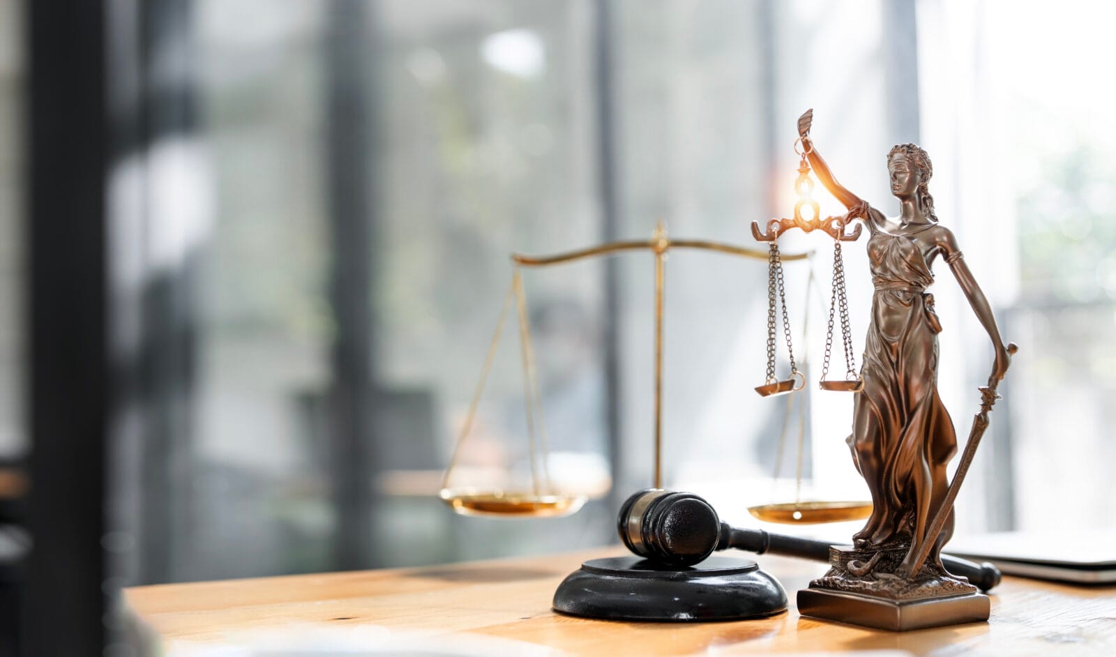 Statue of Lady Justice holding scales and a sword beside a judge’s gavel on a desk.
