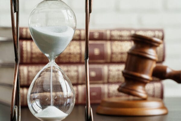 Hourglass with flowing sand beside a judge’s gavel and law books.