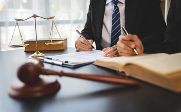 Two personal injury lawyers reviewing legal documents on a clipboard with a gavel, law books, and scales of justice on the desk.
